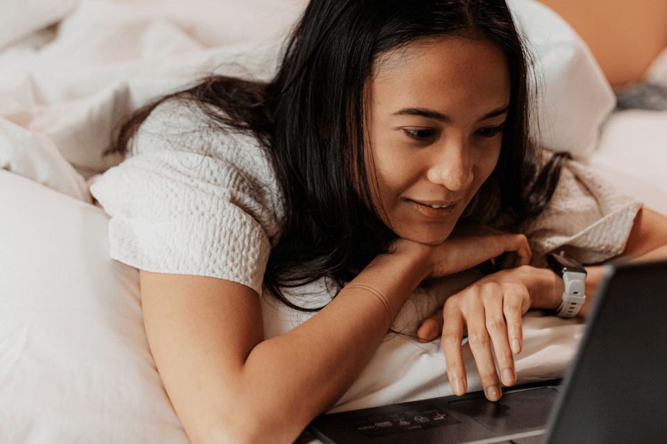 Young Filipina Girlfriend Lying in Bed Using Her Laptop to Communicate with Western Men