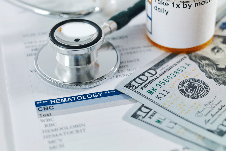Dollar Bills, Pill Bottle and Stethoscope on a Medical Report Representing Medical Expenses Exploited in Filipina Dating Scams