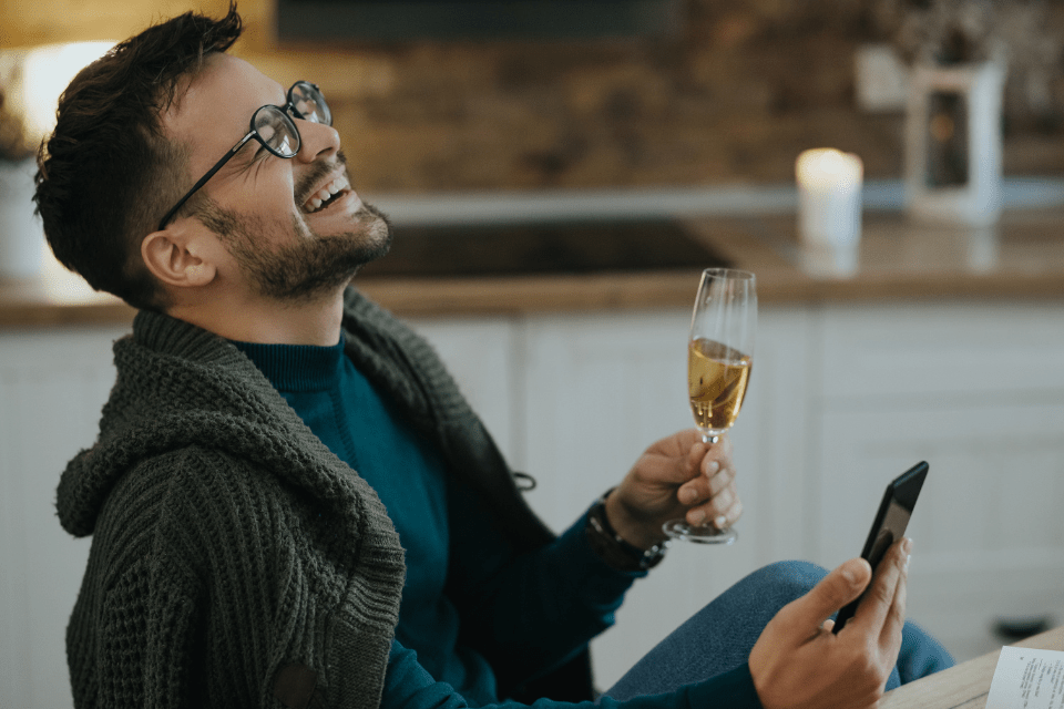 Cheerful foreign man drinking champagne while having a virtual date with a Filipina over his smart phone at home.