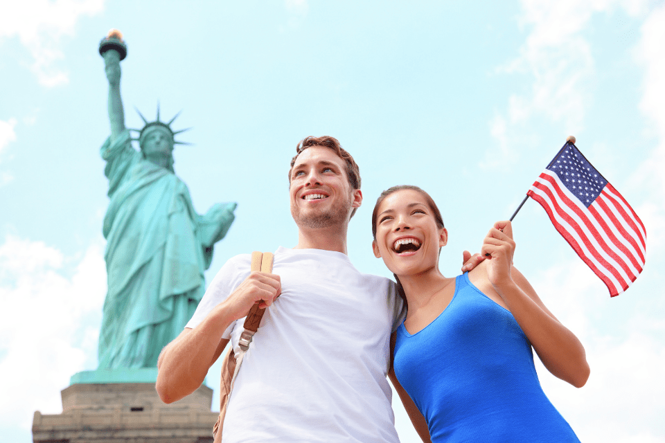 Happy cross-cultural couple on a trip to the Statue of Liberty in New York City, USA. The Filipina is waving the US flag.
