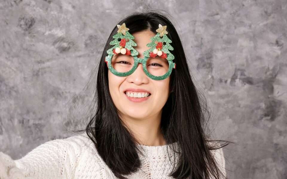 A Filipina woman wearing festive Christmas eyewear and smiling brightly.